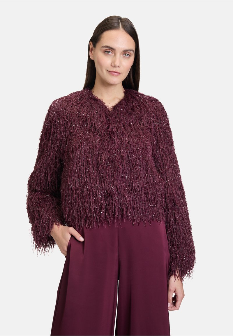 Veste courte bourgogne avec une surface texturée et shaggy. Présente des manches longues et un col simple. Associée à un pantalon ample assorti.