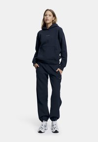 Navy blå hettegenser og matchende joggebukser, begge laget av myk stoff, med kengurulomme, med en liten logo på brystet.