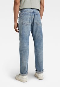 Ljusblå denimjeans med en avslappnad passform, med två bakfickor och subtila blekningar. Uppvikta benslut visar en krämfärgad sneaker.