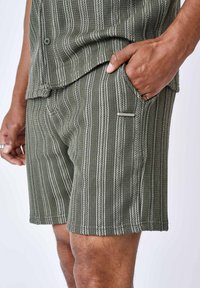 Pantaloni corti verdi a righe realizzati in tessuto strutturato, con una tasca laterale e un piccolo dettaglio metallico sul davanti.