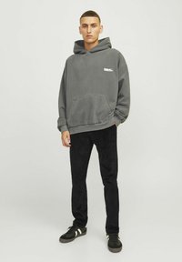 Gray cotton hoodie with front pocket and ribbed hem, paired with black corduroy pants and black sneakers with white stripes.
