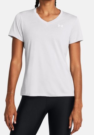 Femme portant un t-shirt blanc uni à col V et manches courtes, ainsi que des leggings noirs, debout sur un fond blanc.
