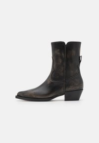 Botte de cow-boy en cuir noir avec un bout pointu, des détails de couture western et un talon empilé. Finition texturée avec un aspect vieilli.