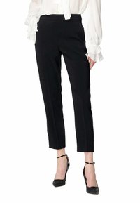 Pantaloni neri su misura dalla vestibilità slim, con una texture liscia e lunghezza a metà polpaccio, abbinati a scarpe nere con tacchi alti.