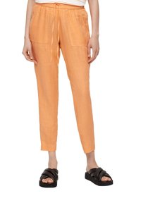 Oranje linnen broeken met een elastische tailleband en trekkoord, voorzien van twee voorzakken en een tapered fit. Draagt met zwarte slide sandalen.