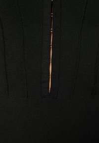 Haut en maille côtelée noire avec un décolleté plongeant, une patte de boutonnage et des coutures horizontales, mettant en valeur un tissu au design texturé.