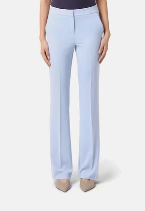 Pantaloni da donna azzurri chiari su misura con tasche frontali, indossati con tacchi beige a punta e top scuro su sfondo bianco.
