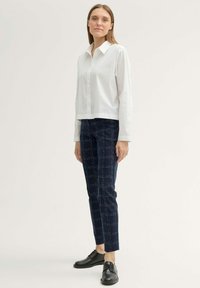 Bílá košile s límečkem, námořnické kostkované kalhoty s bílými švy a černé šněrovací boty. Slim fit, hladký povrch a strukturovaný design.