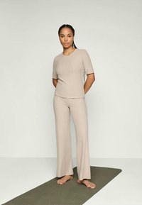 Beige ribbade matchande topp och vida byxor, tillverkade av ett mjukt, stretchigt material. Toppen har korta ärmar och en rund halsringning.