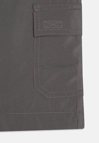Una tela gris con una textura suave presenta un bolsillo cosido en la parte frontal y un detalle de costura a lo largo de los bordes.