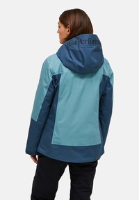 Waterdichte jas in tinten blauw-groen met een gewatteerde capuchon, voorzien van een logo op de achterkant en een contrasterend paneelontwerp.