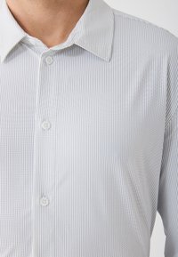 Camicia azzurra e bianca a righe con colletto aperto, caratterizzata da bottoni bianchi e una texture liscia e morbida.