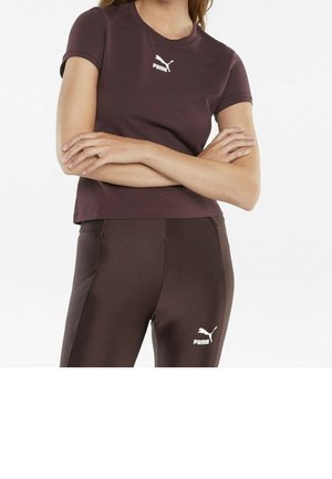 Krótki rękaw, dopasowana fioletowa koszulka sportowa z białym logo Puma. Połączona z gładkimi, brązowymi legginsami również z logo Puma.