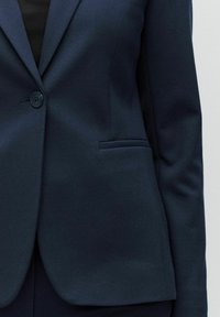 Mörkblå blazer i strukturerad tyg, med en enda knappknäppning och sidoficka. Enkel, skräddarsydd design.