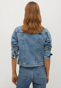 Vaaleansininen farkkutakki, jossa on vartalonmyötäinen muotoilu, käärityt hihat ja hienovaraiset ompeludetaljit. Takakuvassa näkyy klassinen, rento siluetti.