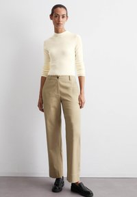 Lichtgele fitted blouse met lange mouwen, gecombineerd met beige high-waisted straight-leg broek en zwarte instappers. Gladde textuur overal.
