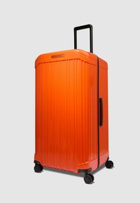 Orangefarbener Hartschalenkoffer mit vertikalen Rillen, einem Teleskopgriff und vier schwarzen Rollen für Mobilität. Verfügt über einen seitlichen Griff für einfaches Anheben.