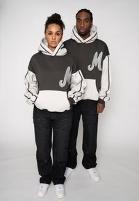 Hanorace în gri închis și alb, cu litera „M” cusută, prevăzute cu buzunar tip cangur. Modelele poartă pantaloni din denim negru și adidași albi.