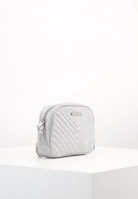 Borsa rettangolare argento con un motivo a zig zag testurizzato, chiusura a zip e dettagli in metallo sulla parte anteriore. Design compatto.