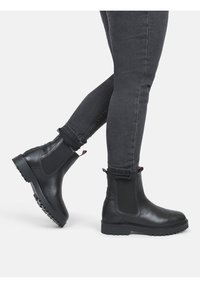 Czarne botki Chelsea z elastycznymi panelami bocznymi, teksturowaną skórą i wytrzymałą gumową podeszwą. Nogawki lekko podwinięte, odsłaniające dopasowane czarne dżinsy.