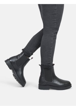 Sorte Chelsea-støvler med elastiske sidepaneler, tekstureret læder og en robust gummisål. Bukserne er lidt oprullede, og afslører slim-fit sorte jeans.