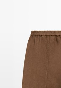 Jupe en tissu marron avec une ceinture élastique et une couture verticale visible au centre, sur fond blanc.