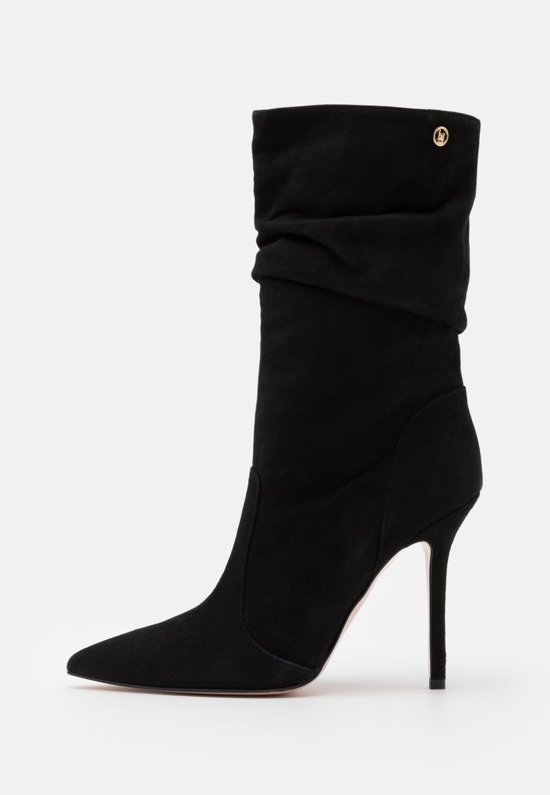 Bottine en daim noir avec un bout pointu et un talon haut en stilettos, présentant un design froissé et un accent doré près du dessus.