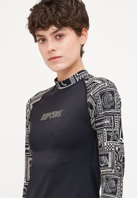 Crna dugoslijeda majica za zaštitu od sunca s uzorkom na rukavima koji prikazuje školjke i motive oceana; uključuje "Ripcurl" branding na prsima.