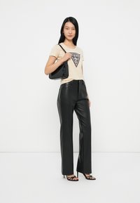 Camiseta beige con logo negro, combinada con pantalones de cuero negros y un pequeño bolso negro. Sandalias de tacón completan el conjunto.