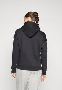 Sweatshirt com capuz preto e corte descontraído, apresentando riscas laterais brancas em contraste e uma textura suave. Combinado com calças de fato cinzentas.