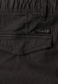 Poche arrière d'un pantalon noir pour hommes avec un rabat et une petite étiquette "Street One Men Ultimate Comfort" au-dessus de la poche.