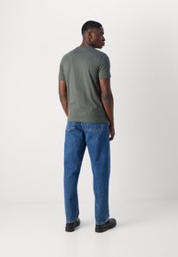 Tricou scurt cu mânecă, de culoare verde închis, ajustat pe corp, asortat cu blugi lejeri din denim albastru și pantofi negri. Textură de material neted, stil minimalist.