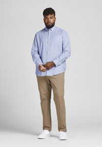 Himmelblaues, langärmliges Hemd mit Knopfverschluss und Brusttasche, kombiniert mit beigen Chinos und weißen Sneakers. Glattes Material, lockere Passform.