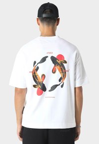Witte katoenen t-shirt met een grafisch beeld van koi-vissen in zwart en oranje, met rode accenten. Lossere pasvorm, korte mouwen en ronde hals.