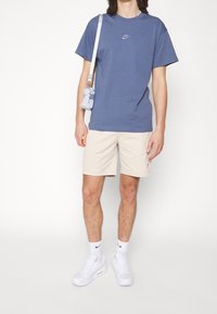Blue cotton T-shirt with a small Nike logo, beige shorts, white sneakers, and a light blue shoulder bag. Casual outfit with minimal details.
