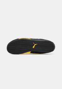 La suola nera delle sneakers presenta una superficie in gomma testurizzata, dettagli gialli e un emblema con il logo. Progettata per garantire trazione e durata.