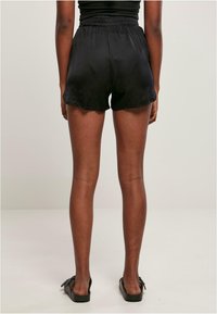 Shorts en satin noir avec une taille élastique, présentant une coupe ample et un ourlet incurvé. Le fond est neutre et l'éclairage est doux.