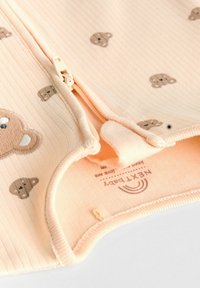 Soft peach-colored baby garment with a ribbed texture, featuring small brown bear patterns, a zip closure, and a soft lining inside.