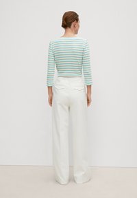 Gestreiftes, kurzes Oberteil in Weiß mit türkisfarbenen Linien, kombiniert mit hochtaillierten, weiten weißen Hosen. Glatte Textur, einfaches Design.
