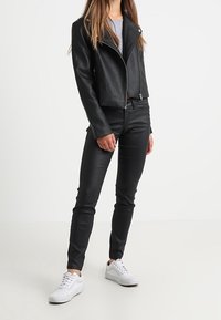 Giubbotto da biker in finta pelle nera con zip argentate, abbinato a pantaloni neri aderenti e sneaker bianche. Tessuto liscio, design corto.