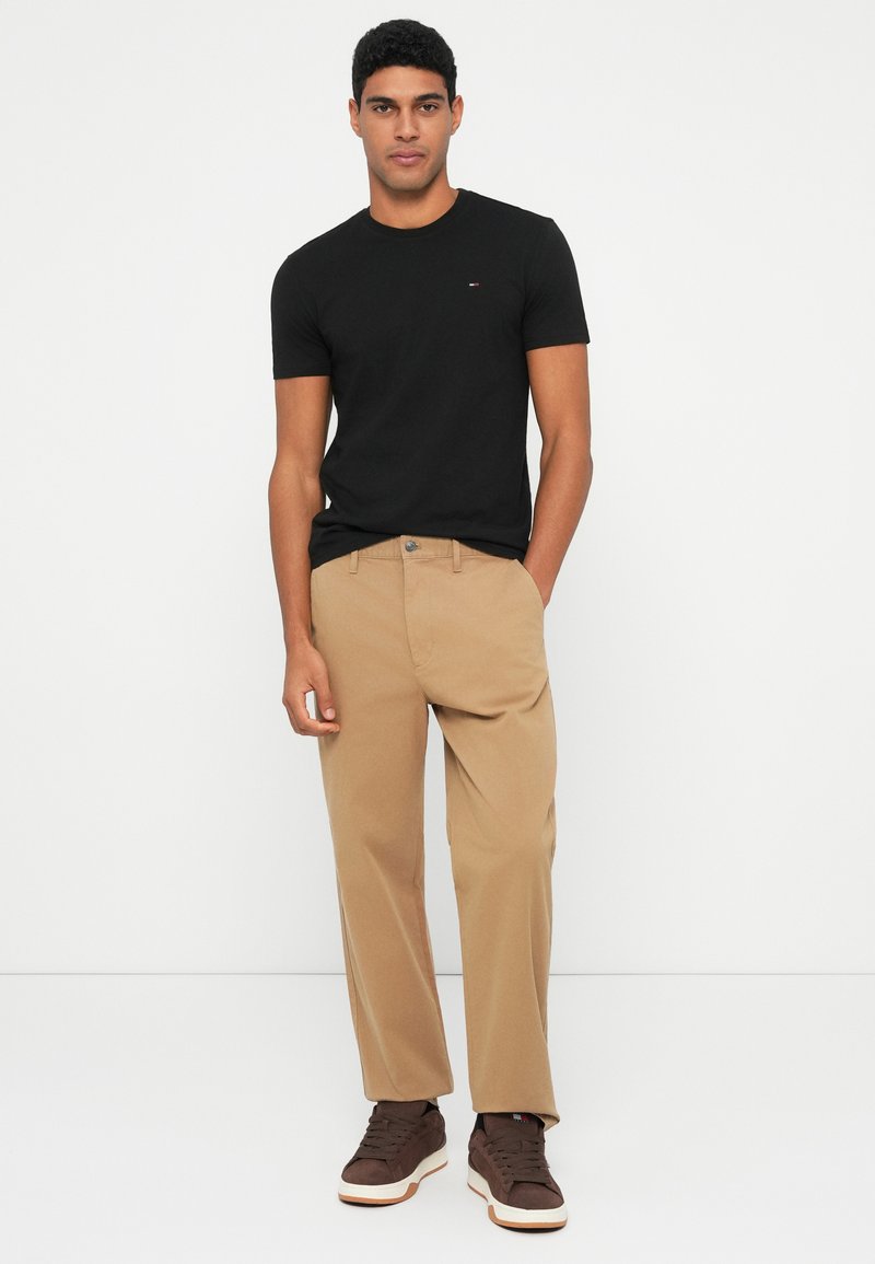 Black crew neck t-shirt, khaki chinos with a straight fit, and brown sneakers with white accents, standing on a plain background.