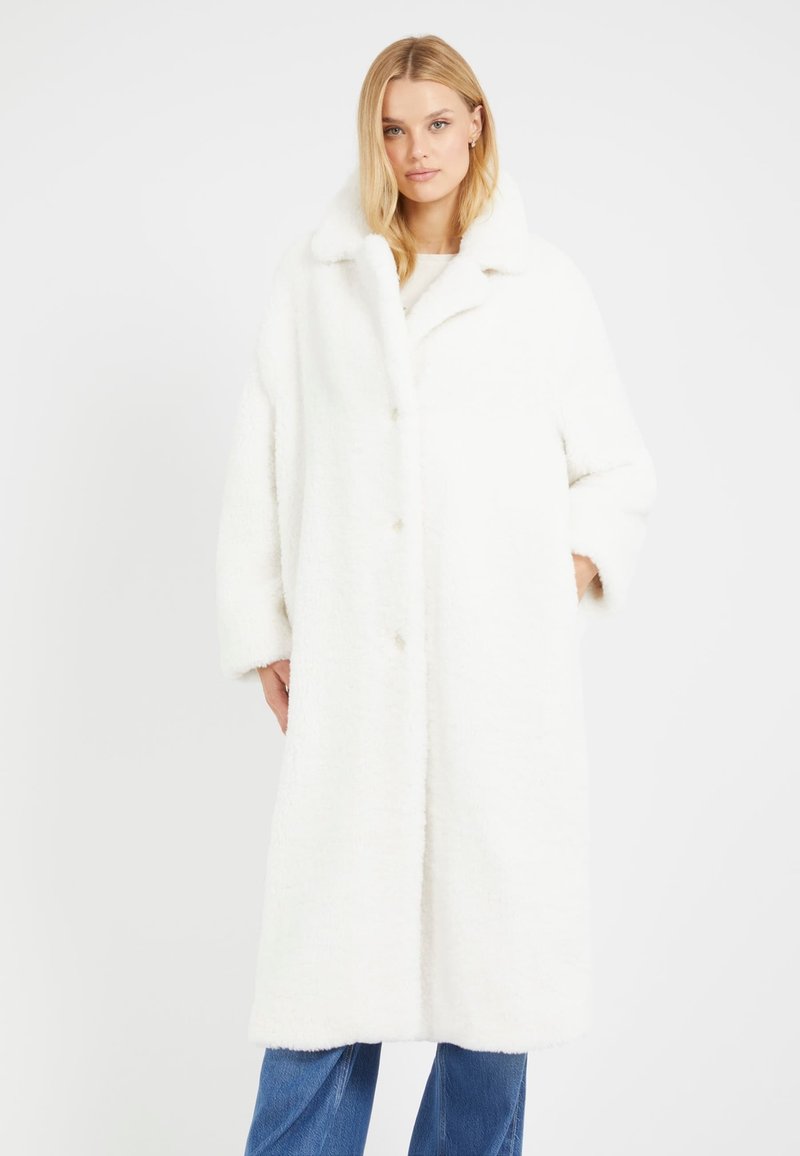 Cappotto oversize bianco realizzato in tessuto peloso, con colletto classico, chiusura a bottoni e tasche laterali, abbinato a jeans blu.