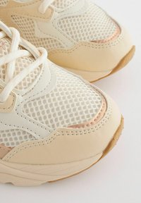 Helle beigen Sneaker aus Mesh- und Leder-Materialien, runder Form, tonalem Stich und einem metallischen Roségold-Akzent.