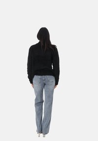 Maglione nero texturizzato con maniche lunghe, abbinato a jeans dritti blu chiaro e stivali con tacco argento. Visto da dietro.