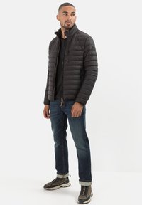 Sort puffet jakke med ståkrave, vandret quiltet design, lynlåslukning foran, båret over en sort skjorte og blå jeans, parret med sneakers.