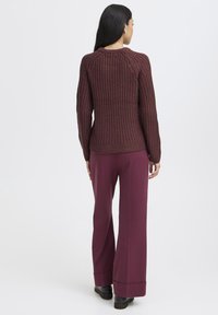 Weinroter gestrickter Pullover mit geripptem Muster und langen Ärmeln, kombiniert mit weiten weinroten Hosen und schwarzen Schuhen.