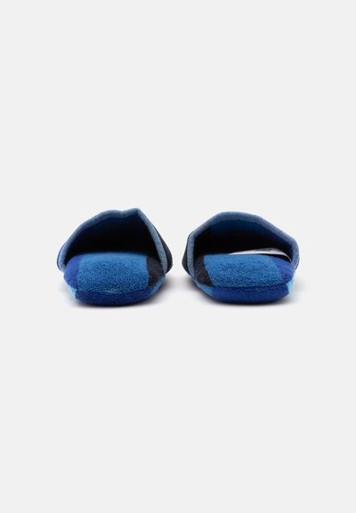 Paire de chaussons à carreaux bleu et noir, ouverts à l’arrière, vus de face sur un fond blanc uni.