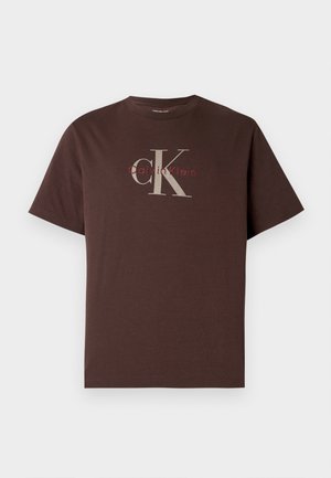Pruun lühikeste varrukatega puuvillane T-särk, millel on suur hall "CK" logo ja väiksemad punased "Calvin Klein" tekstid. Lihtne, lõdvestunud lõikega disain.