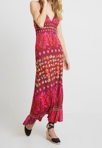 Maxi dress featuring a vibrant floral pattern in shades of pink, orange, and green, with a ruffled hem and spaghetti straps.