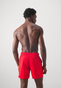 Bermuda da nuoto rossa con una cintura elastica, caratterizzata da una texture liscia e un design semplice. L'immagine si concentra sul retro e sui lati.